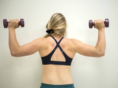 Güçlü beyaz kadın ağırlıkları ile onun bikeps ve omuz kasları üzerinde çalışan egzersizleri yapıyor