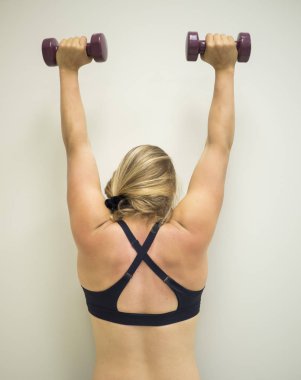 Genç aktif kadın spor salonunda havada ağırlıkları ile bir kol Presi yapıyor