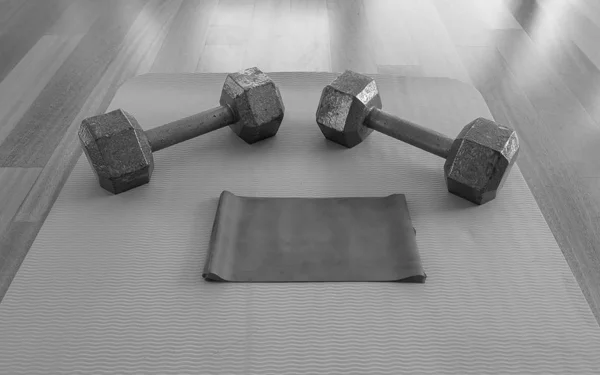 Black and white version of Dumbbells and Exercise band on a Yoga Mat for a Home workout