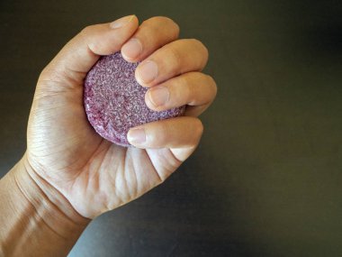 Hand grasping a red Shampoo bar before washing their hair in the shower version 1 clipart