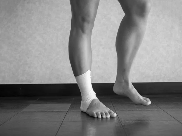 Black and white version of Athlete performing mobility exercises on injured ankle with a tape job