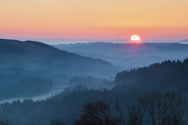 Sun is rising on the horizon over a valley in the Scottish borders
