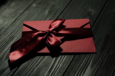 RED GIFT ENVELOPE FOR A SPECIAL HOLIDAY ON A BLACK WOODEN BACKGROUND clipart