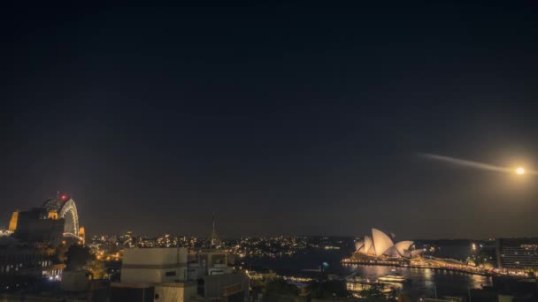 悉尼港的时光流逝在夜间与悉尼歌剧院和悉尼海港大桥的标志性建筑 明亮的月亮穿越晴朗的天空 — 图库视频影像