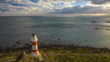 Güzel Cape Palliser deniz feneri Yeni Zelanda. Güzel bir akşam Timelapse video çekim dağınık bulutlar ile ışık ve hiç mevcut güçlü rüzgarların neden olduğu dalgalanmalar su.