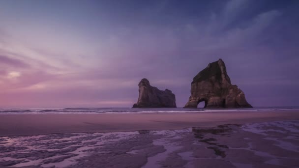 ロマンチックな夜の美しい色に沖の岩に自然なアーチを持つ壮大な空のビーチ Wharariki ビーチ ニュージーランド タイムラプス ビデオ — ストック動画