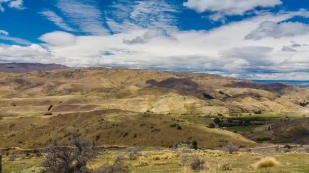 田舎の上空の雲の白のパッチでタイムラプスの日当たりの良い夏の日のビデオの乾燥した丘の風景 ニュージーランドの南の島での撮影 — ストック動画