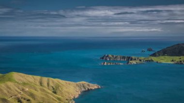 Spectacular coastline of New Zealand in timelapse video on sunny day with blue ocean and typical green hills.