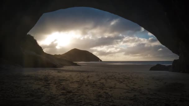 劇的な雲が空を横切って渡す洞窟の入り口から美しいビーチで夕日のタイムラプス ビデオ — ストック動画