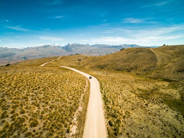 Yeni Zelanda doğal çakıl yol. Orta Otago bölgesinde tipik kurak manzara Güney Alpson ufuk karlı zirveleri ile. Başlık towrds dağlar Backpackers hava atış van.