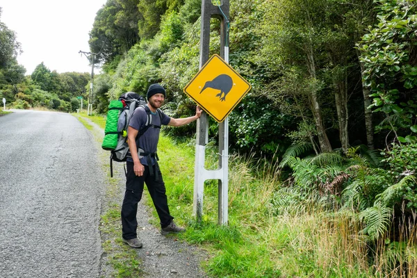 Happy young backpacker with Kiwi bird sign on Stewart Island in New Zealand, popular place with tourists for spotting Kiwi birds.