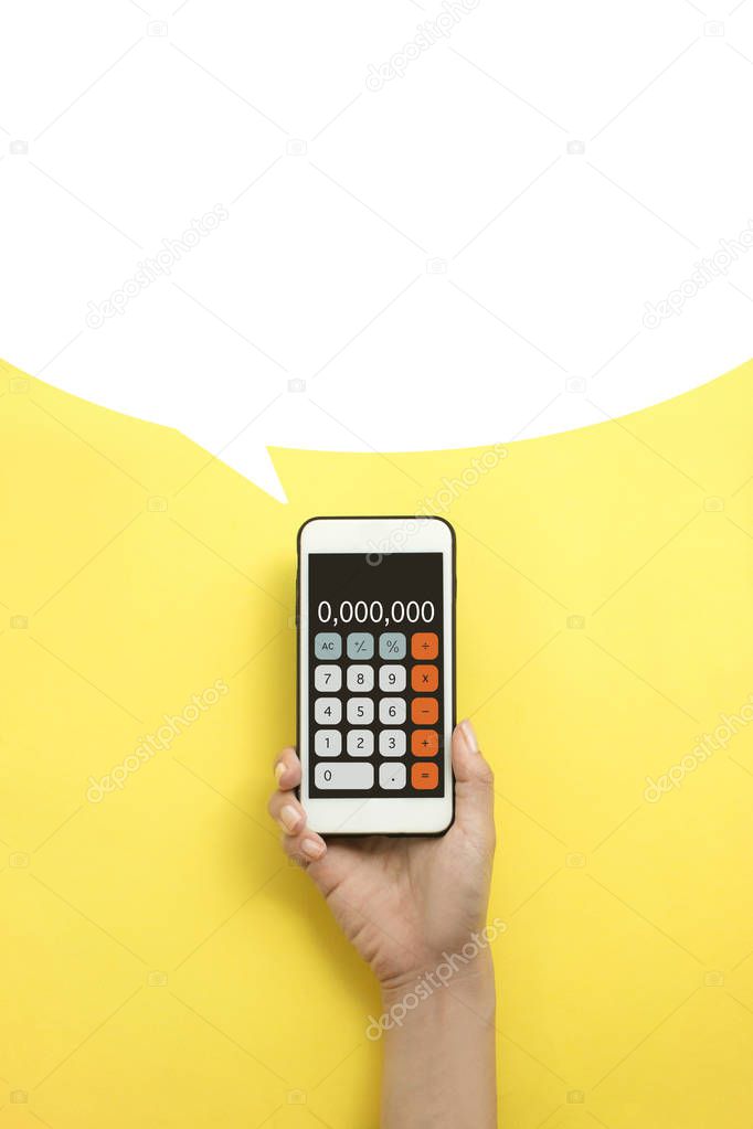 Flat lay hand holding mobile phone calculator with speech bubble on yellow background.