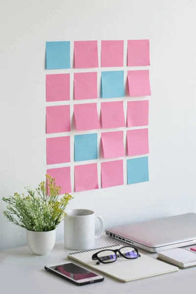 Well organised blank sticky notes on office desk wall.