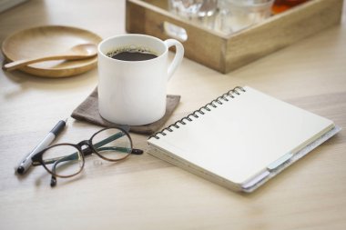 Close up one coffee cup with black coffee and blank note book page on table top.