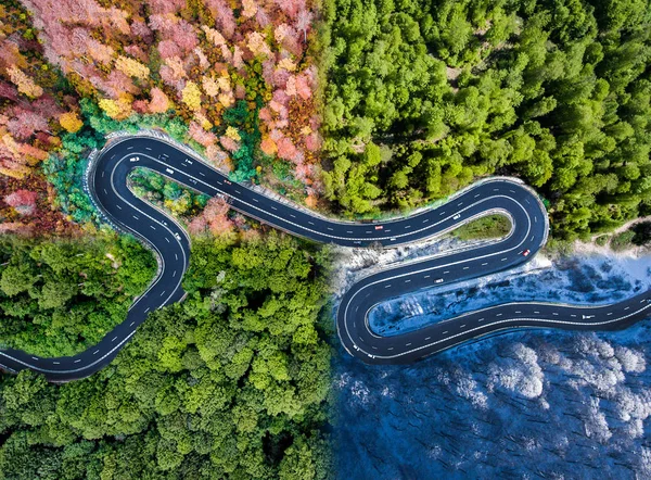 Winding road in all four seasons. Aerial view of a curved highway trough the forest. Composite drone roadway weather image
