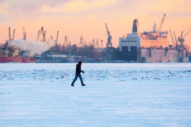 Kış. Şehir manzarası. Bir adam limanın arka planında buzda yürür.