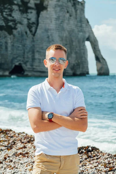 Portrait of a young successful man on the background of sky and sea landscape. Blonde with glasses in white shirt