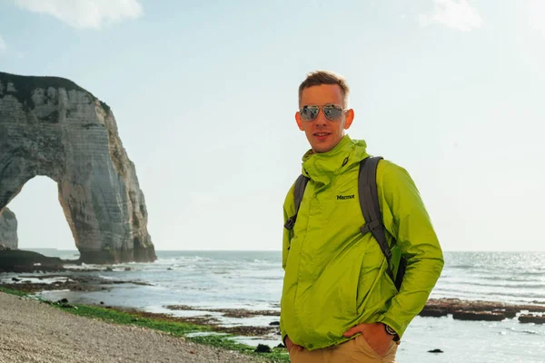 Portrait of a young successful man on the background of sky and sea landscape. Blonde with glasses in green jacket