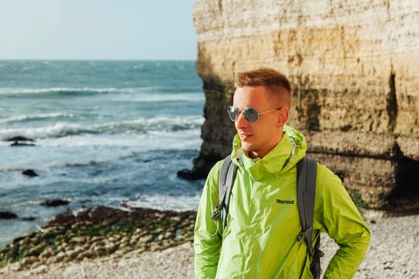 Portrait of a young successful man on the background of sky and sea landscape. Blonde with glasses in green jacket