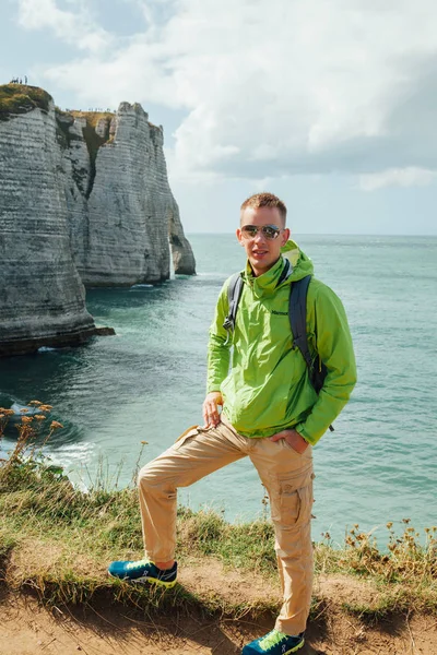 Portrait of a young successful man on the background of sky and sea landscape. Blonde with glasses in green jacket