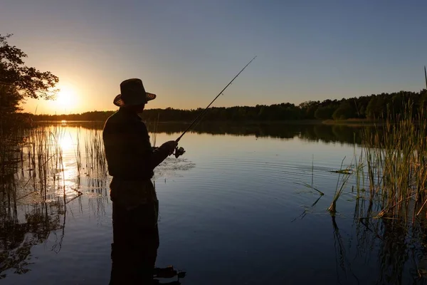 渔夫的剪影在湖中站立和捉住鱼在日落期间 — 图库照片
