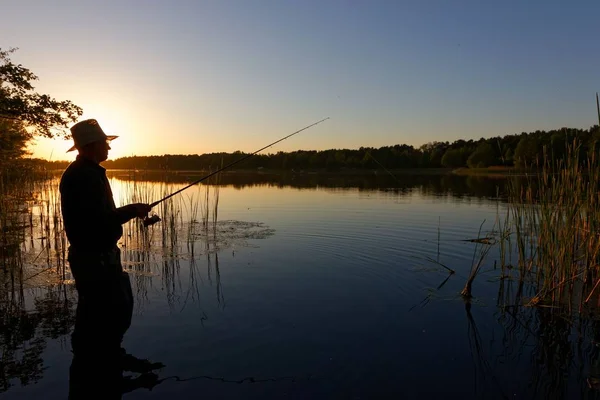 渔夫的剪影在湖中站立和捉住鱼在日落期间 — 图库照片