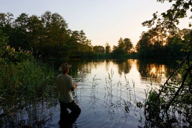 Gölde ayakta ve günbatımı sırasında balık yakalamak balıkçı