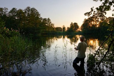 Gölde ayakta ve günbatımı sırasında balık yakalamak balıkçı