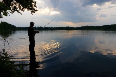 Bulutlu gün batımı sırasında balık yakalamak balıkçı silüeti