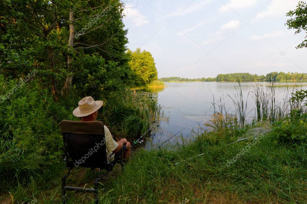 Fisherman sitting on the chair and fishing on the shore of a lake during sunny day
