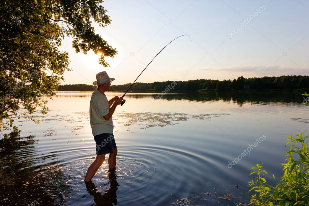 Angler standing in a lake and catching the fish during sunset