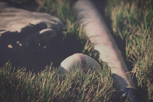 Baseball im Gras mit Schläger und Handschuh im Hintergrund. — Stockfoto