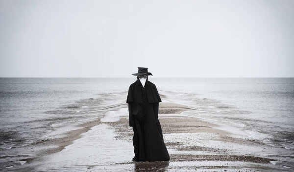 Plague doctor in seaside. Outdoor portrait with dramatic sky in background.