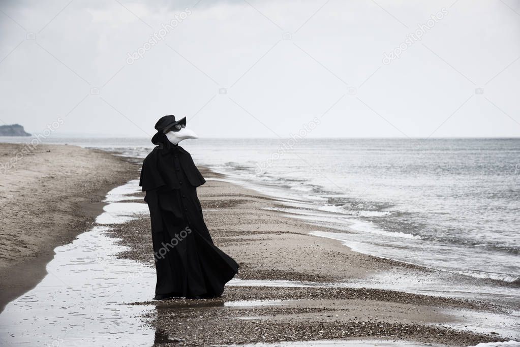 Plague doctor in seaside. Outdoor portrait with dramatic sky in background.