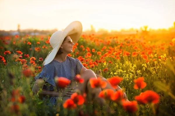 夕阳西下 戴着大帽子的小女孩坐在罂粟地里 — 图库照片
