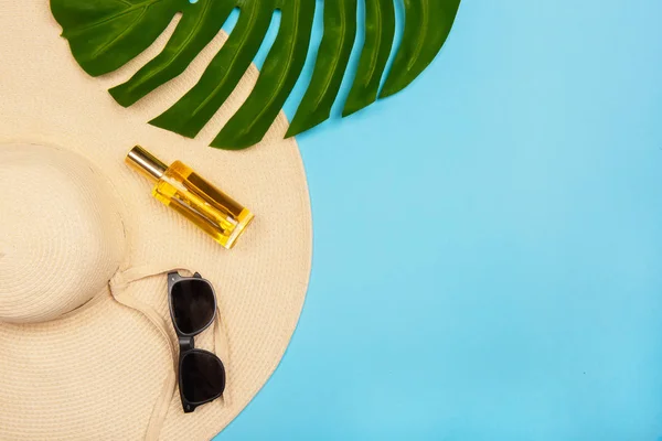 Flache Fotosonnenhut, gelbe Sonnenschutzflasche, Sonnenbrille und Monstera-Blatt auf blauem Pastellgrund. Damenaccessoires für den Strandurlaub — Stockfoto