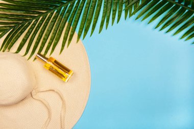 Düz yatıyordu fotoğraf güneş şapkası, sarı güneş kremi şişesi ve palmiye yaprakları mavi bir pastel arka plan üzerinde. Plaj tatilleri için kadın aksesuarları