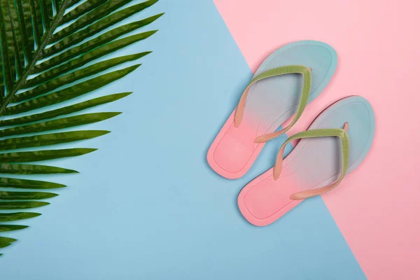 Stylische Strand-Flipflops auf rosa und blauem Pastellhintergrund mit Palmblatt, Draufsicht. Sommerkonzept mit Kopierraum. lizenzfreie Stockbilder