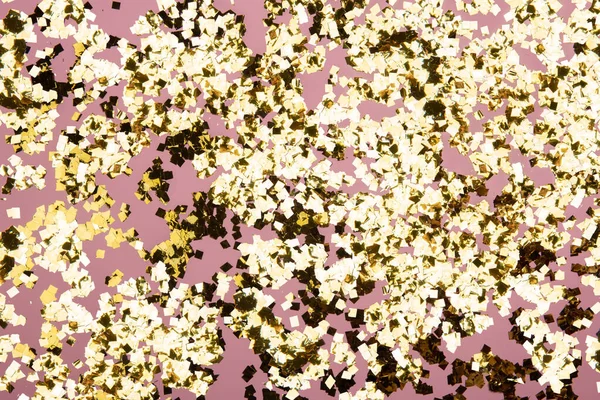 Golden confetti glitter on pink background. Festive holiday pastel backdrop. Greeteng cards template. Flat style composition.