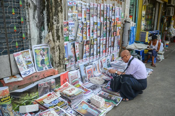 Yangon, Myanmar - 25 Nisan 2016: Yangon bir sokakta Newpapaper gazete bayi de okuma unidentifiled Birmanya adam