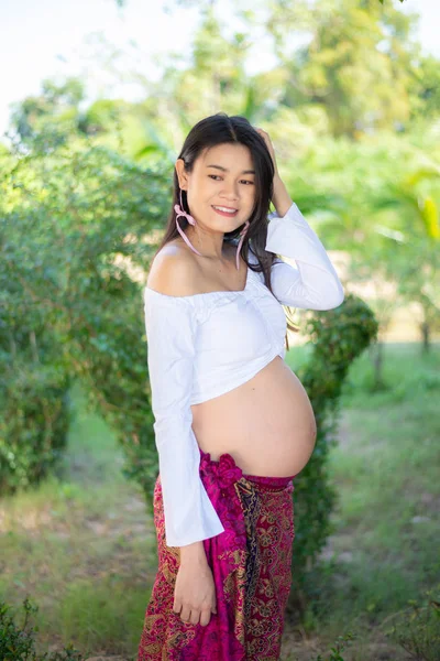 Young Asian beautiful pregnant woman in white dress touching her belly — Stock Photo, Image