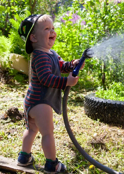 Divertente ragazzino che gioca con il tubo da giardino nel cortile soleggiato. Bambino prescolare divertendosi con spruzzi d'acqua. Attività estive all'aperto per bambini . — Foto Stock