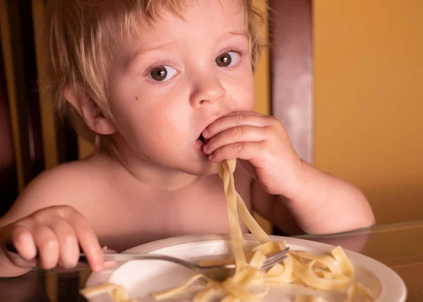 A criança na cozinha à mesa comendo macarrão e vista interessante do topo — Fotografia de Stock