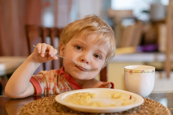 Criança na cozinha comendo salsicha e purê de batatas — Fotografia de Stock