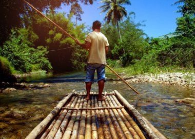 Nehre bambu salını kullanmak için direk kullanan adam. Tayland Chiang Mai eyaletinde turizm için kariyer biri.Jungle ve arka plan olarak mavi gökyüzü ile dağlar.