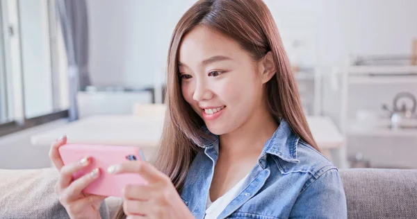 woman sitting  on sofa and playing  mobile phone happily at home