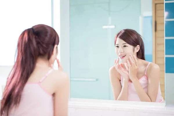 美容女性の鏡で見ていると バスルームで彼女の頬に触れる — ストック写真