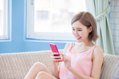 woman sit on sofa and use phone happily at home clipart