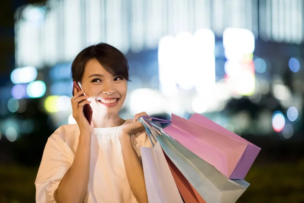 woman speak phone happily and take shopping bag at night