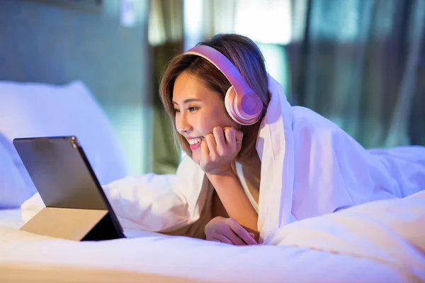 woman watch a video by digital tablet and wear headset on the bed at night